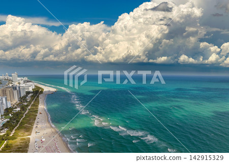 Miami Beach city with high luxury hotels and condos and sandy beachfront. High angle view of tourist infrastructure in southern Florida, USA Miami Beach city with high luxury hotels and condos and sandy beachfront. High angle view of tourist infrastructure in southern Florida, USA 142915329