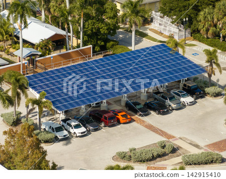 Solar power generation technology integrated in urban infrastructure. Photovoltaic panels installed as shade roof over parking lot with parked cars for effective production of clean energy. Solar power generation technology integrated in urban infrastructure. Photovoltaic panels installed as shade roof over parking lot with parked cars for effective production of clean energy. 142915410