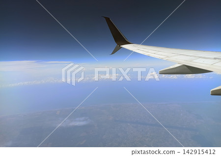 View through airplane window of commercial jet plane wing flying high in the sky. Air travelling concept View through airplane window of commercial jet plane wing flying high in the sky. Air travelling concept 142915412