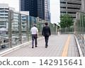 Two businessmen walking on a pedestrian deck; a scene from an office district. 142915641