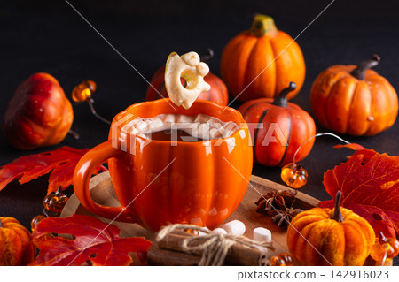 Cozy autumn beverage with pumpkin mug, marshmallows, and cinnamon sticks for holiday celebration Cozy autumn beverage with pumpkin mug, marshmallows, and cinnamon sticks for holiday celebration 142916023