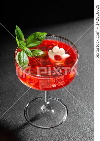 Creative red cocktail garnished with basil and fun ice shape in glass on dark background Creative red cocktail garnished with basil and fun ice shape in glass on dark background 142916029
