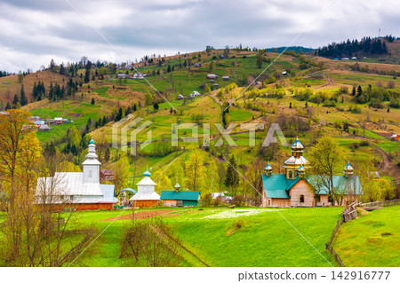 agricultural field on hillside in mountains near village in dappled light. wooden fence on the slope. Synevyr national park, TransCarpathia, Ukraine. cloudy sky in springtime agricultural field on hillside in mountains near village in dappled light. wooden fence on the slope. Synevyr national park, TransCarpathia, Ukraine. cloudy sky in springtime 142916777