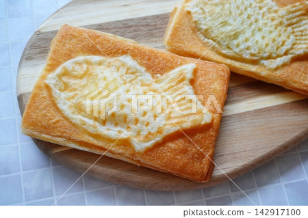 A snack consisting of golden-brown, fish-shaped taiyaki-style pies arranged on a wooden plate. 142917100