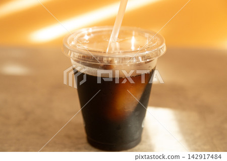 A black coffee in a plastic cup with a straw stuck in it. 142917484