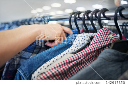 Hand browsing secondhand clothing on rack at thrift shop with mi Hand browsing secondhand clothing on rack at thrift shop with mi 142917850