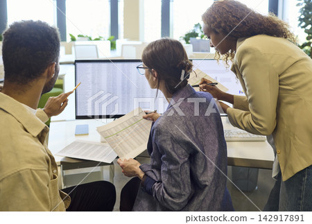 Colleagues analyzing data at computer in office meeting, planning report review Colleagues analyzing data at computer in office meeting, planning report review 142917891