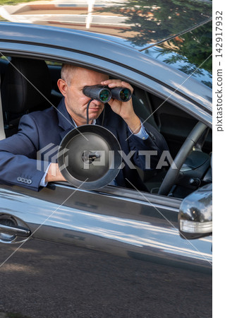 Private investigator follows a target from a car while using binoculars and a sensitive directional microphone to gather information. Private investigator follows a target from a car while using binoculars and a sensitive directional microphone to gather information. 142917932