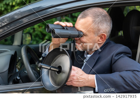 Private detective listening to a target from a car during covert investigation Private detective listening to a target from a car during covert investigation 142917935