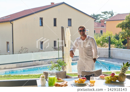 Man in White Relaxing by Private Pool with Breakfast Table on Sunny Villa Terrace Man in White Relaxing by Private Pool with Breakfast Table on Sunny Villa Terrace 142918143