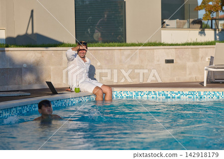 Man Working With Laptop at Poolside While Child Swims on Sunny Summer Vacation Man Working With Laptop at Poolside While Child Swims on Sunny Summer Vacation 142918179