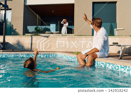 Family Waving From Villa Poolside During Summer Vacation Morning At Luxury Home Balcony Family Waving From Villa Poolside During Summer Vacation Morning At Luxury Home Balcony 142918242