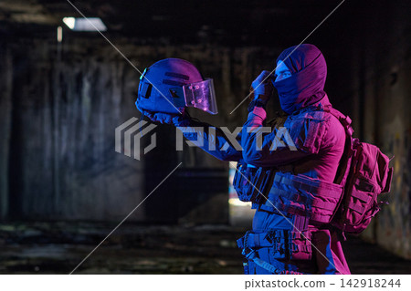 Tactical Soldier In Balaclava Holding Helmet Inside Dark Abandoned Urban Building With Neon Light Tactical Soldier In Balaclava Holding Helmet Inside Dark Abandoned Urban Building With Neon Light 142918244