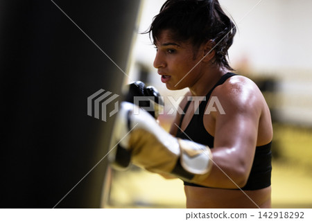 Female Boxer Training in Gym Hitting Heavy Bag With Gloves During Intense Workout Session Female Boxer Training in Gym Hitting Heavy Bag With Gloves During Intense Workout Session 142918292