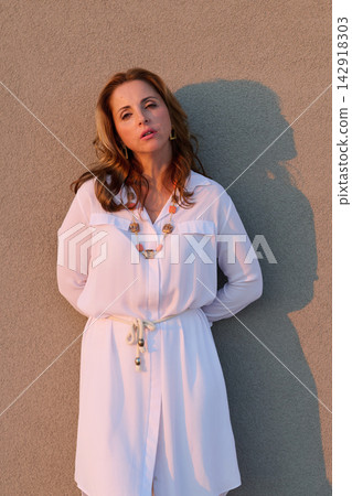 Woman in White Dress Leaning Against Textured Wall at Golden Hour Wearing Necklace Woman in White Dress Leaning Against Textured Wall at Golden Hour Wearing Necklace 142918303