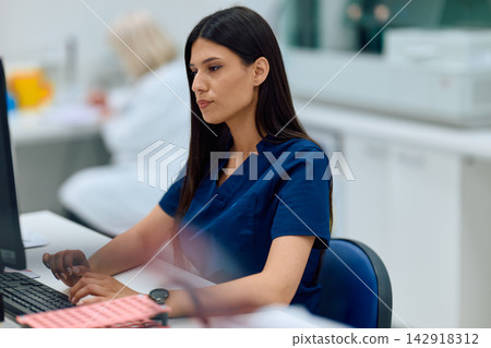Medical professional focused on computer work in a clinical setting during the day shift Medical professional focused on computer work in a clinical setting during the day shift 142918312