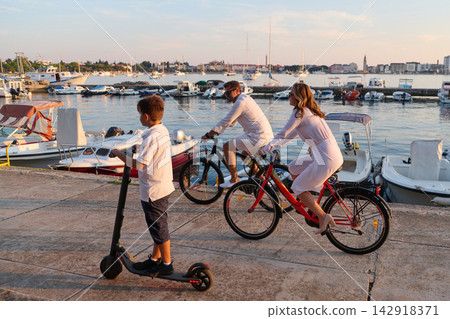 Family Cycling and Scooter Ride Along Umag Harbor at Sunset With Boats and Summer Atmosphere Family Cycling and Scooter Ride Along Umag Harbor at Sunset With Boats and Summer Atmosphere 142918371