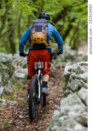 Mountain biking cyclist riding a trail through a green forest with backpack and helmet Mountain biking cyclist riding a trail through a green forest with backpack and helmet 142918483