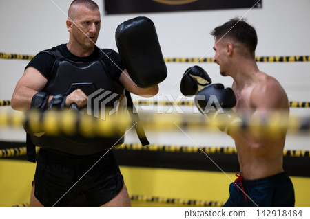 Boxer Training With Coach Holding Pads During Intense Boxing Padwork Session In Gym Ring Boxer Training With Coach Holding Pads During Intense Boxing Padwork Session In Gym Ring 142918484