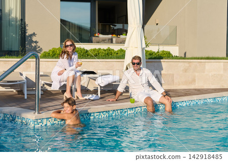 Family Relaxing by Luxury Pool on Vacation Enjoying Sunshine, Drinks and Leisure at Modern Villa Family Relaxing by Luxury Pool on Vacation Enjoying Sunshine, Drinks and Leisure at Modern Villa 142918485
