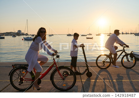 Family Cycling and Scooting at Sunset by the Harbor With Parents and Child Enjoying Seaside Ride Family Cycling and Scooting at Sunset by the Harbor With Parents and Child Enjoying Seaside Ride 142918487