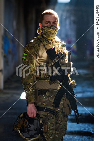 Masked Soldier In Camouflage Tactical Gear Holding Rifle And Helmet In Urban Setting Masked Soldier In Camouflage Tactical Gear Holding Rifle And Helmet In Urban Setting 142918489