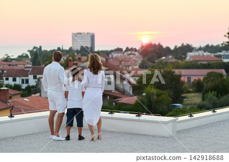 Family On Rooftop Terrace Watching Sunset Over Coastal Town And Sea View Family On Rooftop Terrace Watching Sunset Over Coastal Town And Sea View 142918688