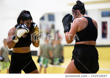 Two Female Boxers Sparring During Intense Boxing Training Session In Indoor Gym With Coach Two Female Boxers Sparring During Intense Boxing Training Session In Indoor Gym With Coach 142918697