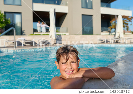 Smiling Boy Relaxing At Hotel Poolside On Summer Vacation With Balcony And Loungers In Background Smiling Boy Relaxing At Hotel Poolside On Summer Vacation With Balcony And Loungers In Background 142918712