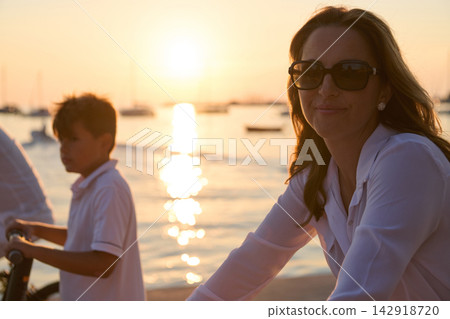Woman And Boy Cycling By Harbor At Sunset Wearing Sunglasses During Summer Evening Leisure Woman And Boy Cycling By Harbor At Sunset Wearing Sunglasses During Summer Evening Leisure 142918720