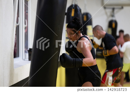 Determined Woman Boxing Workout at Busy Gym Training With Punching Bag and Boxing Gloves Determined Woman Boxing Workout at Busy Gym Training With Punching Bag and Boxing Gloves 142918723