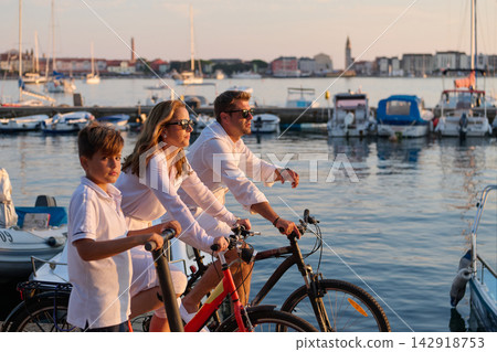 Family Biking Along Marina at Sunset With Parents and Child by Boats in Harbor 142918753