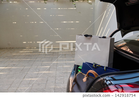 Shopping Bags and Luggage in an Open Car Trunk on a Sunny Driveway Ready for Travel 142918754