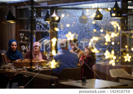 Family Dinner Celebration With Women Wearing Headscarves And Laughing Child In Festive Restaurant Family Dinner Celebration With Women Wearing Headscarves And Laughing Child In Festive Restaurant 142918759