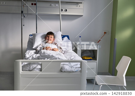 Smiling child resting in a hospital bed during a calm afternoon in a pediatric ward Smiling child resting in a hospital bed during a calm afternoon in a pediatric ward 142918830