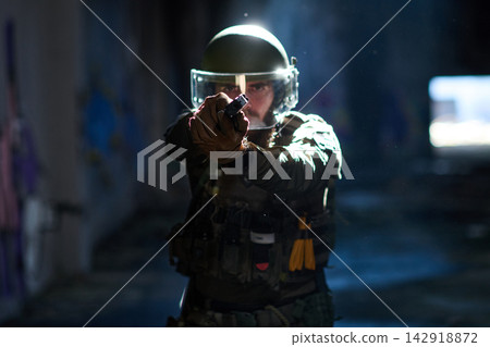 Armed Tactical Officer in Riot Gear Aiming Handgun During Night Operation in Urban Building Armed Tactical Officer in Riot Gear Aiming Handgun During Night Operation in Urban Building 142918872
