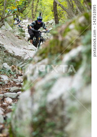 Mountain biker riding a rocky forest trail with helmet camera and protective gear Mountain biker riding a rocky forest trail with helmet camera and protective gear 142918995