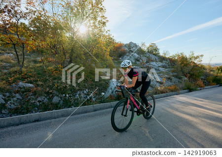 Female Cyclist Training on Scenic Road at Sunrise on Autumn Hillside Female Cyclist Training on Scenic Road at Sunrise on Autumn Hillside 142919063