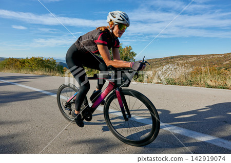 Female Cyclist Training On Road Bike In Aerodynamic Position Through Scenic Countryside Female Cyclist Training On Road Bike In Aerodynamic Position Through Scenic Countryside 142919074