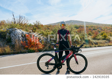 Female Cyclist Standing With Time Trial Bike on Scenic Autumn Road During Training Female Cyclist Standing With Time Trial Bike on Scenic Autumn Road During Training 142919105