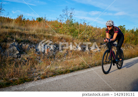 Female Cyclist Training on a Rural Road at Sunset Road Cycling Fitness and Endurance 142919131