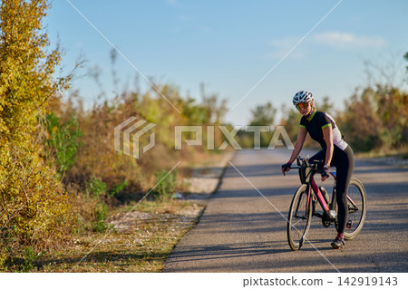 Female Cyclist Riding Road Bike On Quiet Country Road During Sunny Outdoor Training Session 142919143