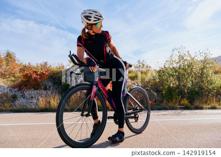 Female Cyclist On Road Bike Resting During Outdoor Training Ride In Scenic Countryside Female Cyclist On Road Bike Resting During Outdoor Training Ride In Scenic Countryside 142919154