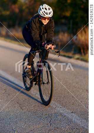 Female Cyclist Training On Road Bike During Golden Hour Outdoor Fitness Ride In Countryside Female Cyclist Training On Road Bike During Golden Hour Outdoor Fitness Ride In Countryside 142919178