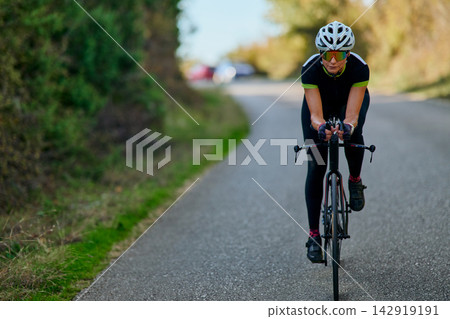 Female Cyclist Training On Rural Road On Road Bike Wearing Helmet And Cycling Gear Female Cyclist Training On Rural Road On Road Bike Wearing Helmet And Cycling Gear 142919191