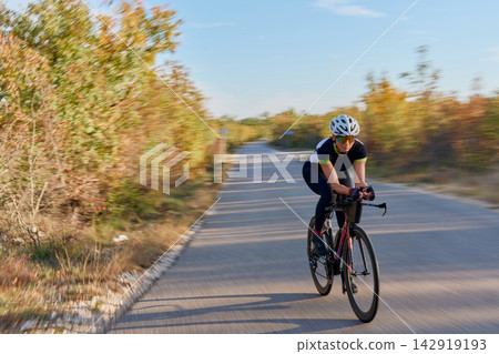 Female Cyclist Riding Road Bike Fast on Country Road During Autumn Training Ride 142919193