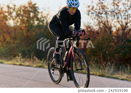 Female Cyclist Training On Road Bike At Sunrise In Autumn Speed, Endurance And Fitness Female Cyclist Training On Road Bike At Sunrise In Autumn Speed, Endurance And Fitness 142919196