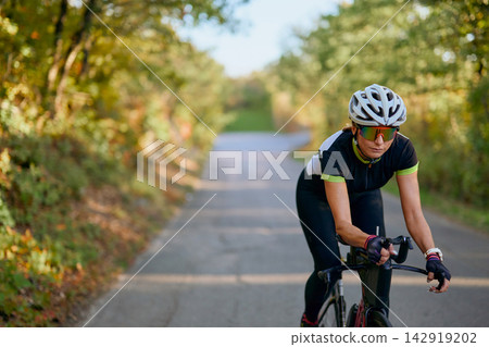 Female Road Cyclist Training Outdoors On Country Road Wearing Helmet And Sports Sunglasses Female Road Cyclist Training Outdoors On Country Road Wearing Helmet And Sports Sunglasses 142919202