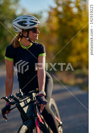 Female Cyclist On Road Bike Wearing Helmet And Sunglasses During Outdoor Training Ride At Sunset Female Cyclist On Road Bike Wearing Helmet And Sunglasses During Outdoor Training Ride At Sunset 142919225