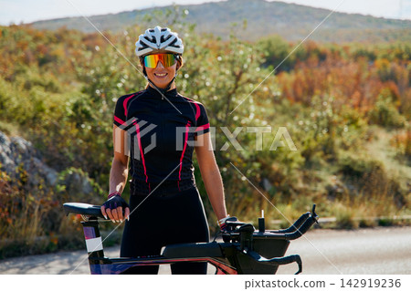 Female Cyclist Smiling Beside Her Time Trial Bike On A Sunny Rural Road During Training Female Cyclist Smiling Beside Her Time Trial Bike On A Sunny Rural Road During Training 142919236